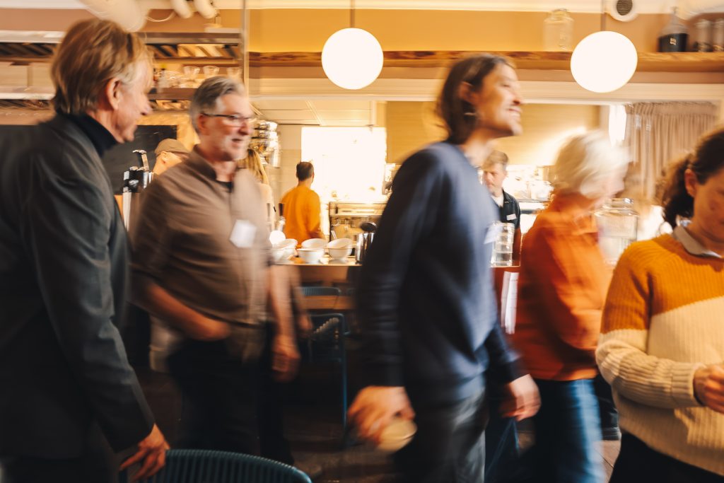 Blurred cafe interior with several people standing and talking, warm lighting.